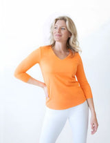JudyP - Woman wearing an orange long-sleeve top and white pants on a white background