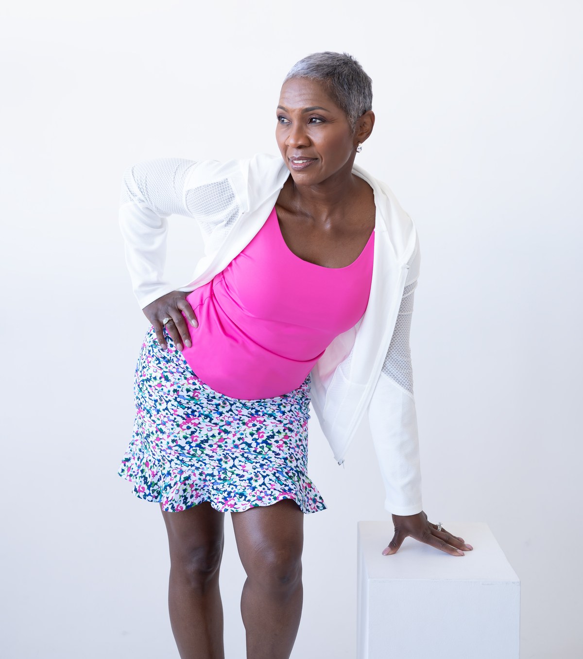 Woman in a pink JudyP Stephanie scoop tank with a white court jacket and printed skort