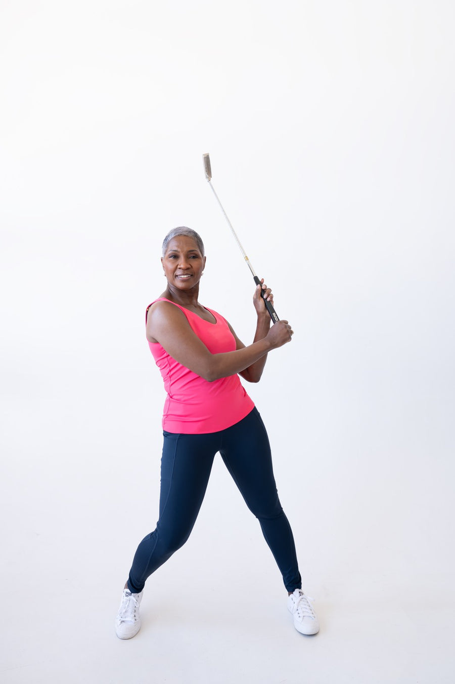Woman mid golf swing in a pink JudyP sleeveless top