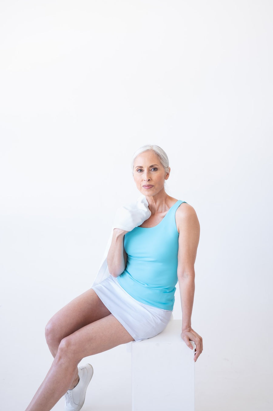 Woman in an aqua JudyP tank and white tennis skirt with a towel over her shoulder